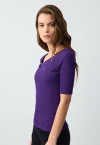 Top viola a coste con maniche corte, caratterizzato da un collo a giro e un bottone decorativo sul lato sinistro della spalla. Texture liscia.