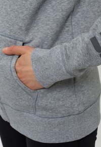 Sudadera con capucha gris que cuenta con un bolsillo frontal, puños y dobladillo acanalados, hecha de un material suave con una textura sutil.