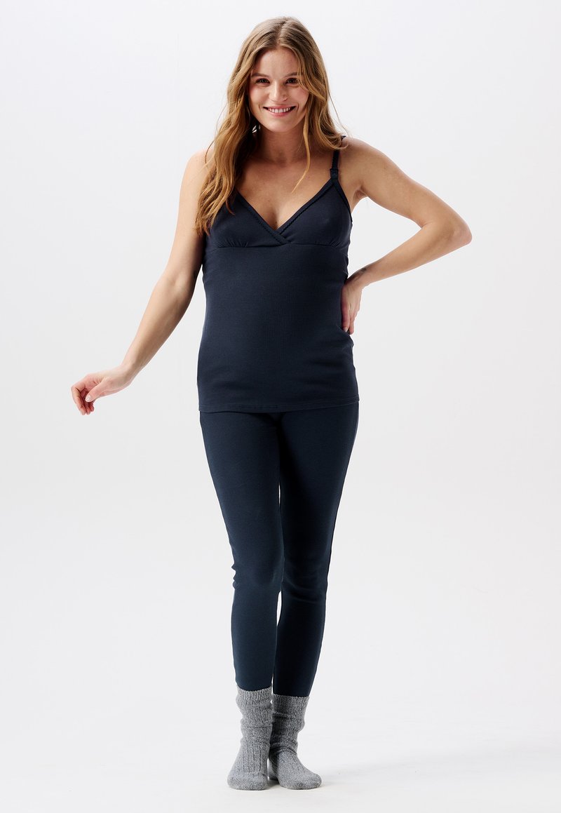 Navyblauwe geribbelde tanktop met een V-hals, gecombineerd met bijpassende strakke leggings. Model draagt grijze gebreide sokken, wat een casual uitstraling geeft.