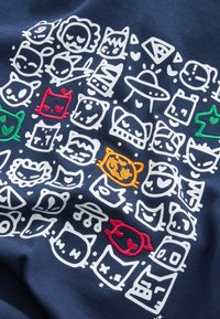 Volti e sagome di animali cartoni animati bianchi con quattro volti colorati ricamati su tessuto blu navy, inclusi gatti, cani e un UFO.