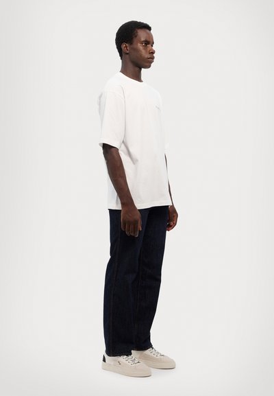 Hvid bomulds t-shirt med korte ærmer og rund hals, parret med mørkeblå jeans og hvide sneakers. Enkeltdesign, ingen mønstre.
