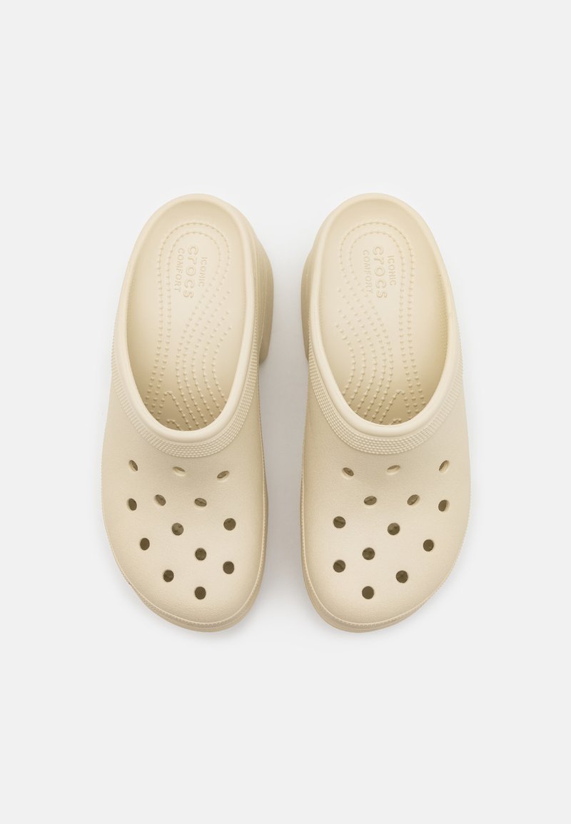 Zuecos beige con forma redondeada, hechos de un material ligero. Presentan agujeros perforados y una plantilla texturizada para mayor comodidad.