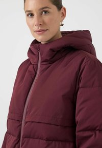 Mørkerød boblejakke med høy krage og hel glidelås, med glatt stofftekstur og horisontale sømdetaljer.