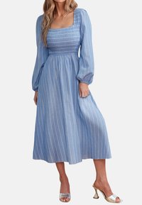 Vestido largo a rayas azules con escote cuadrado, cuerpo fruncido y mangas amplias; combinado con tacones plateados de punta abierta.