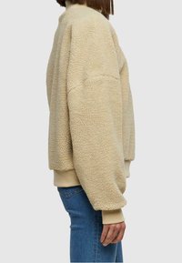 Beige Fleece-Pullover mit strukturiertem Oberflächenmaterial, oversized Passform und gerippten Bündchen. Verfügt über einen hohen Kragen und eine lässige, gemütliche Optik.