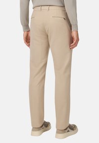 Pantaloni beige a gamba dritta, con due tasche posteriori con zip e una sottile trama, abbinati a scarpe in tessuto grigio.