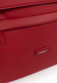 Rode synthetische tas met een gladde textuur, voorzien van een bovenklep en een rechthoekige metalen logo-plaat met de tekst "HEXAGONA."