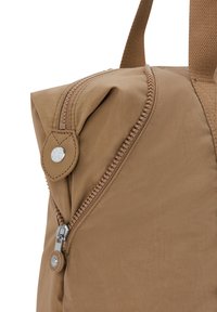 Tan nylon backpack with a curved top, zippered closure, and a leather accent near the zipper featuring a silver snap button. Textured fabric.