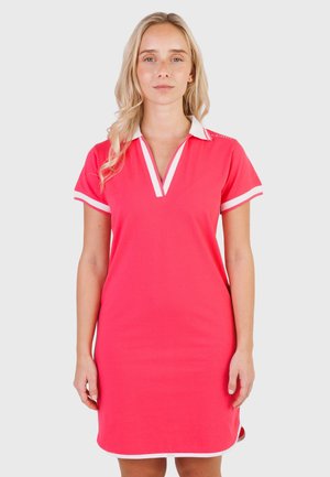Donna che indossa un vestito polo rosa acceso con colletto bianco e bordo delle maniche, in piedi davanti a uno sfondo semplice grigio chiaro.