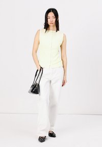 Sleeveless light yellow top with buttons paired with white wide-leg pants. The model holds a small black handbag and wears black shoes.