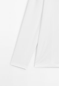 Langärmeliges Hemd aus glattem weißen Stoff, mit lockerem Schnitt und weicher Textur, mit gerade geschnittenem Saum und Manschettendetails.