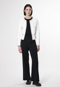 Giacca in pelle bianca con dettagli in neron e borchie nere, tasche con zip e design cropped, abbinata a pantaloni larghi neri e scarpe chunky nere.