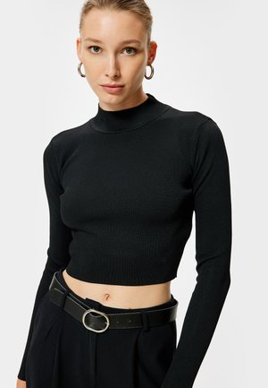 Zwarte geribbelde coltrui met lange mouwen en een cropped ontwerp, gecombineerd met een zwarte riem met een zilveren ronde gesp.