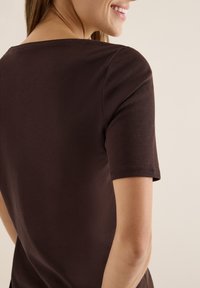 Braunes Baumwoll-T-Shirt mit kurzen Ärmeln, runder Ausschnitt und glatter Textur, von der Seite und hinten betrachtet.