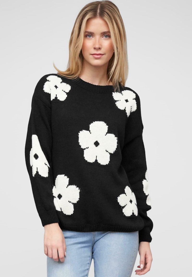 Un pull en tricot noir avec de grands motifs floraux blancs, un col rond et des manches longues, associé à un jean bleu clair.