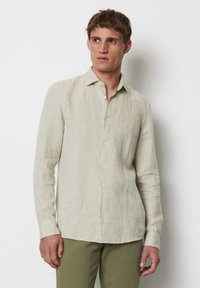 Helle beigefarbene Langarmbluse aus Leinen, mit einem Button-Down-Kragen, subtiler Textur und geradem Saum. Getragen mit olivgrünen Hosen.