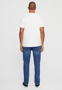 White cotton T-shirt with short sleeves, viewed from the back, paired with blue denim jeans and black sneakers, no prominent details.