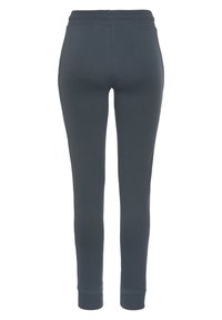 Graue Baumwoll-Jogginghosen, figurbetonter Schnitt, elastischer Bund und gerippte Bündchen. Glatte Textur ohne sichtbare Muster oder Akzente.