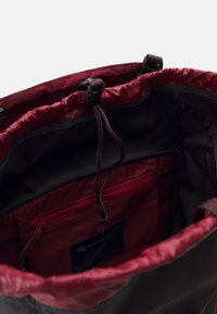Brown and burgundy backpack interior with a smooth fabric texture, drawstring closure, zip pocket, and a label on the inner side.