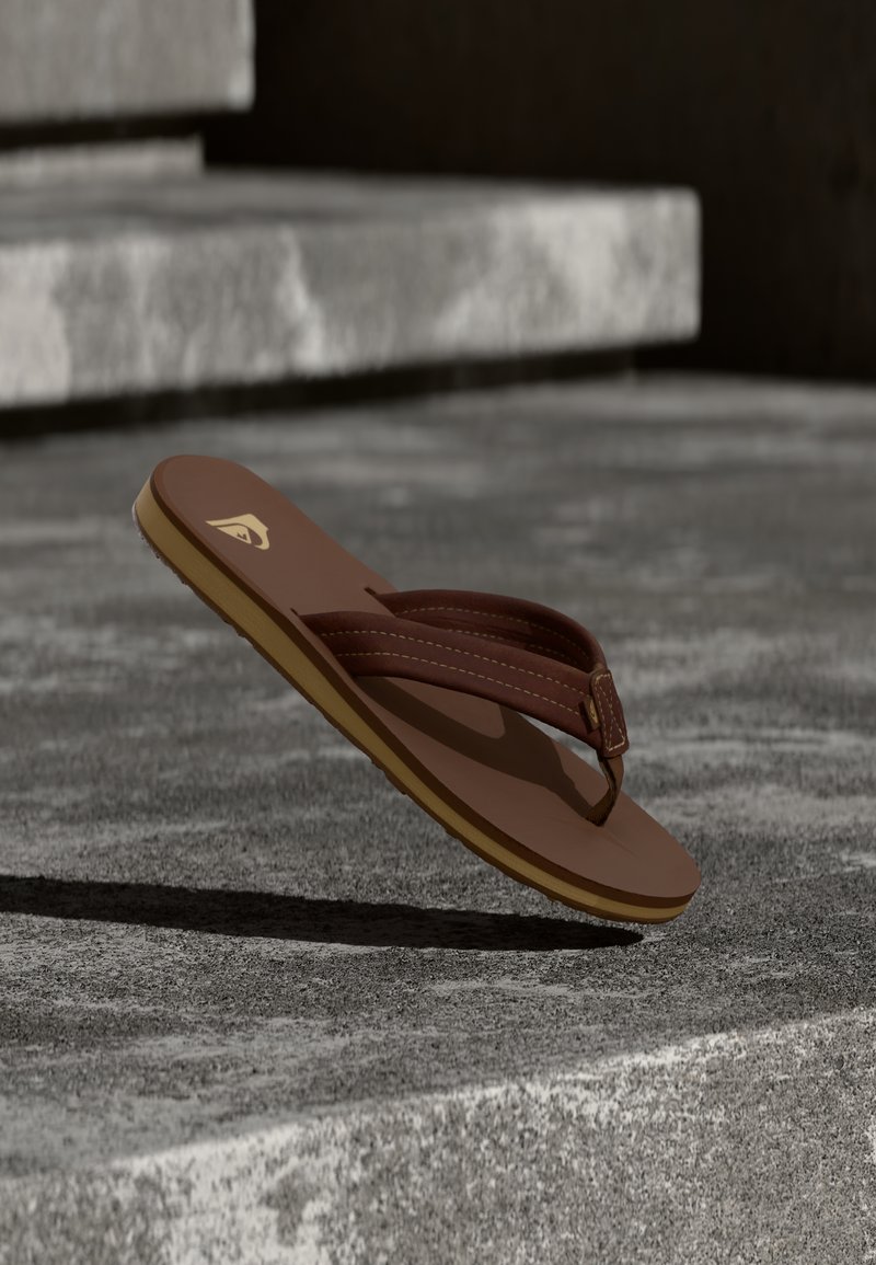 Καφέ σαγιονάρα με κίτρινη σόλα που αιωρείται πάνω από τραχιές σκάλες από σκυρόδεμα σε φυσικό φως.