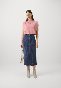 Lys rosa ermeløs topp med rund hals, parret med en mørkeblå denim midi-skjørt med frontlommer og rett snitt.