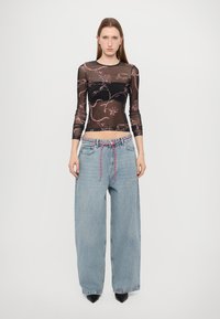 Schwarzes transparentes Langarmoberteil mit floralem Muster; hellblaue weit geschnittene Jeans mit gewebtem Kordelzug und lockerer Passform; High-Heels.