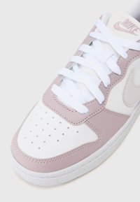 White and light pink sneaker with a perforated toe, white laces, rubber sole, and Nike branding on the tongue and side.