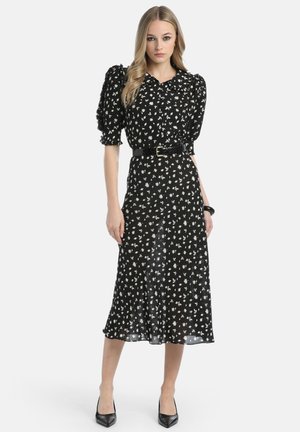 Schwarzes Kleid mit weißem Blumenmuster, Puffärmeln und einem taillierten Bund. Midikleid-Länge mit einem fließenden Saum. Glatte Stofftextur.