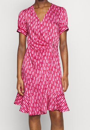 Femme portant une robe portefeuille rose mi-longue avec un motif géométrique, des manches courtes bouffantes et un ourlet volanté.