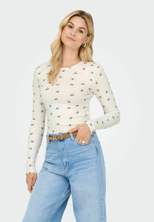 Biały, prążkowany top z długim rękawem i małym kwiatowym wzorem, okrągłym dekoltem oraz falbanowymi mankietami, zestawiony z wysokogatunkowymi jasnoniebieskimi dżinsami i brązowym paskiem.