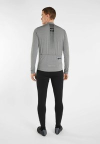 Langærmet grå cykeltrøje med lodrette striber på ryggen, baglomme og sorte detaljer, parret med sorte tætsiddende bukser og cykelsko.