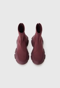 Bottines bourgogne à la surface lisse et extensible, bout rond et semelles en caoutchouc épaisses. Comprend une fermeture éclair à l'arrière.