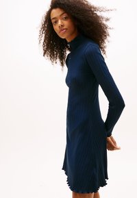 Abito a maniche lunghe a coste blu navy con collo alto, caratterizzato da un orlo smerlato e una silhouette aderente, realizzato in tessuto strutturato.