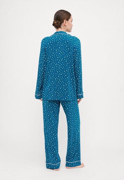 Conjunto de pijama verde-água com padrão de estrelas brancas, apresentando uma parte superior de botão de mangas longas e calças largas. Destaca-se com detalhes em branco.