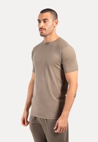 Camiseta de manga corta ajustada en material sintético color marrón claro. Presenta un escote redondo y una textura suave, adecuada para ropa deportiva.