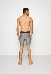 Graue Sportshorts mit eng anliegendem Schnitt, gefertigt aus strukturiertem Stoff, mit einem schwarzen Bund und roten Akzenten. Modell von hinten gezeigt.