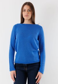 Maglione blu a maglia con maniche lunghe, scollatura rotonda e tessuto texturizzato. Abbinato a jeans in denim scuro, dal design minimalista, senza hardware visibile.