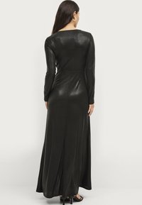Lang zwart jurk met lange mouwen, gemaakt van een glanzend materiaal, met een getailleerde bustier en een vloeiende rok. Zichtbare naaddetails op de rug.