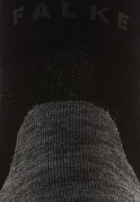 Chaussette noire au toucher lisse, avec un haut en côte et une section de bout grise. Le nom de la marque "FALKE" est imprimé près du poignet.