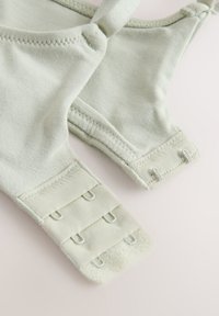 Gros plan de bretelles de soutien-gorge en tissu doux gris clair avec fermetures à agrafes réglables sur une surface unie.