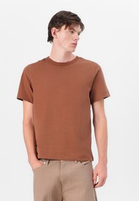 Bruine T-shirt met korte mouwen en ronde hals, gemaakt van zachte katoenen stof. Heeft een rechte snit en subtiele zijsplitten voor extra comfort.