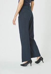 Marine gestreifte weit geschnittene Hose mit hoher Taille, ausgestattet mit einer Gesäßtasche und kombiniert mit eleganten schwarzen High Heels.