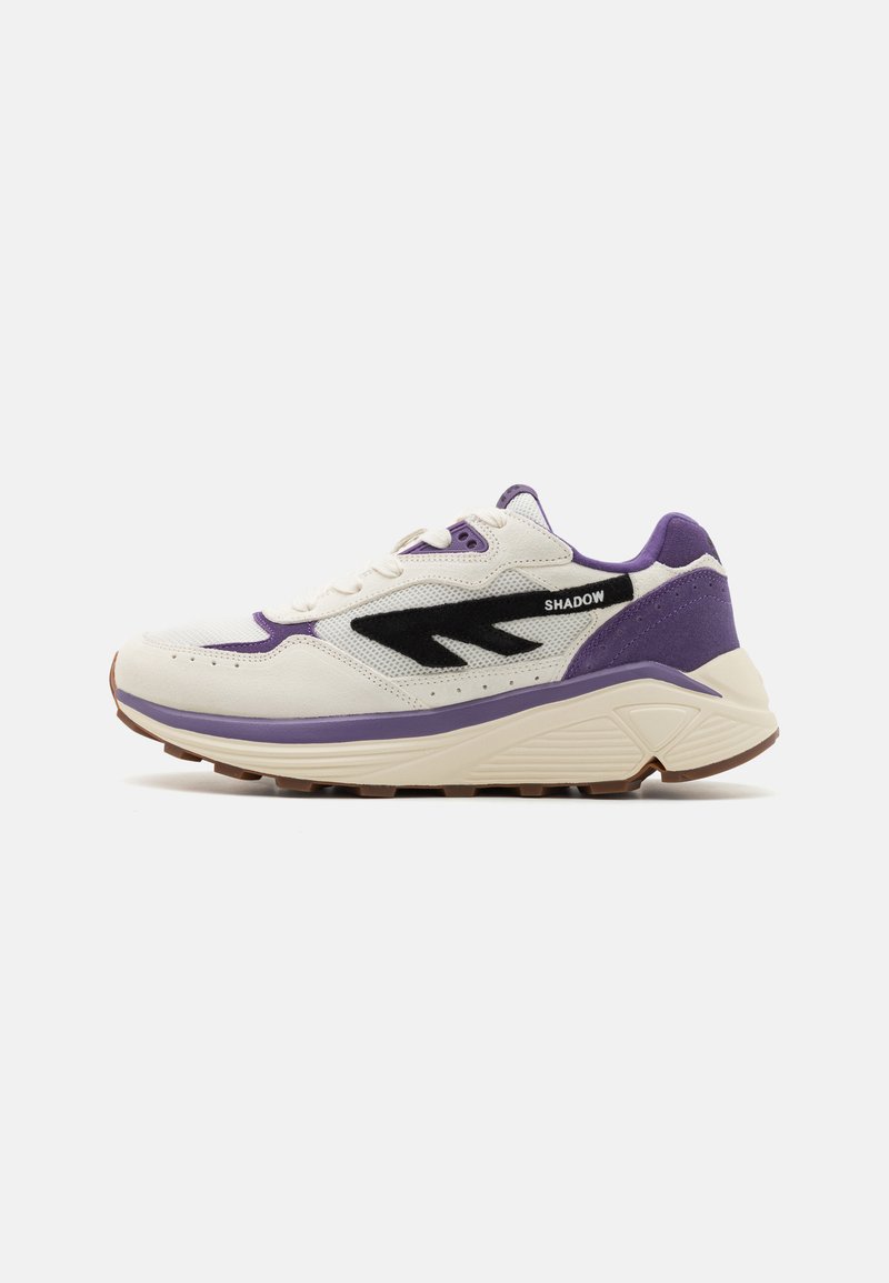 Die Sneakers besitzen ein Obermaterial aus weißem Mesh mit lila und schwarzen Akzenten, eine dicke Sohle und strukturierte Details. Die Markenbezeichnung "SHADOW" befindet sich an der Seite.