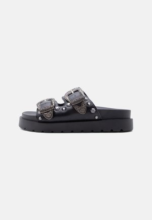 Black slide sandal with thick sole, two wide straps, engraved silver buckles, and decorative metal studs on a plain background.