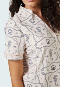 Camicia a maniche corte con bottoni in tessuto beige chiaro, caratterizzata da un motivo nautico con cavallucci marini, delfini e conchiglie in blu navy.