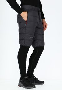 Polstrede shorts i mørkegrå med en quiltet design, lynlåslommer og logo-detalje. Båret over sorte leggings og kombineret med sorte sneakers.