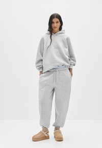 Grauer übergroßer Hoodie mit Raglanärmel, kombiniert mit grauen Jogginghosen mit elastischem Bund. Tragen mit beigen Plattformschlappen.