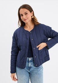 Veste matelassée marine avec un col rond, des boutons-pression, deux poches latérales et une coupe ample, fabriquée en matière synthétique douce.