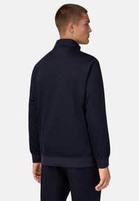 Tamsiai mėlynas užtrauktuku užsegamas džemperis su aukštu apykakle, ilgomis rankovėmis ir elastingais rankogaliais. Pasižymi lygiu paviršiumi ir subtiliu logotipu nugarėlėje.