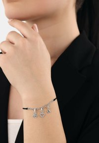 Bracciale in argento con cordino nero, caratterizzato da tre charm: un occhio, un cuore e un pendente rotondo, tutti con pietre preziose trasparenti.